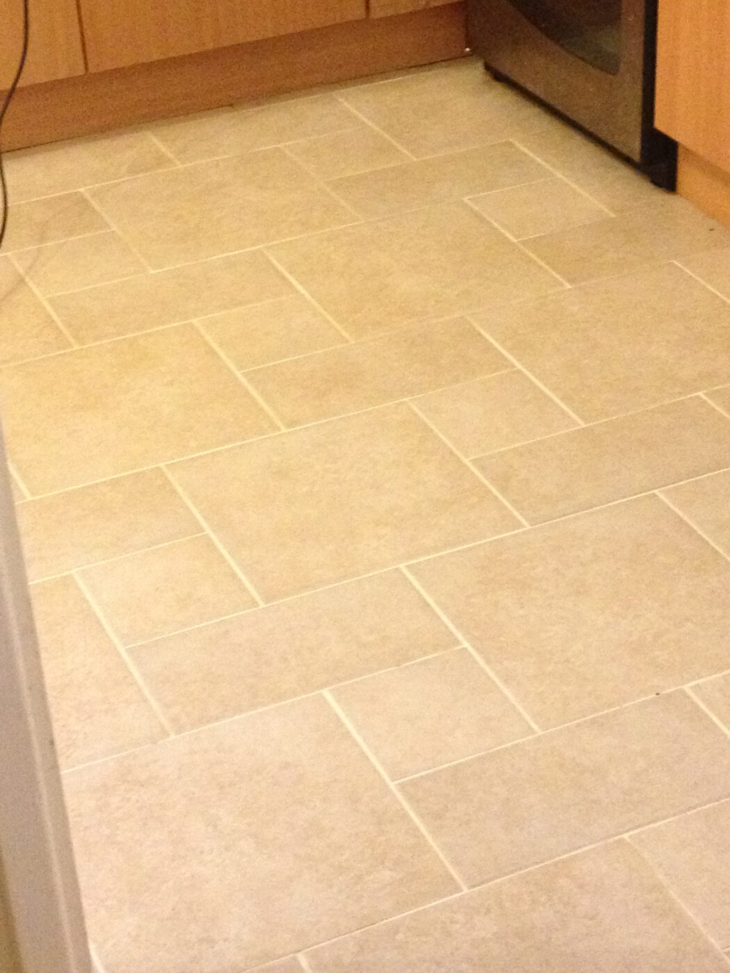 Large cream floor tiles laid in a brick-bond pattern across a kitchen floor.