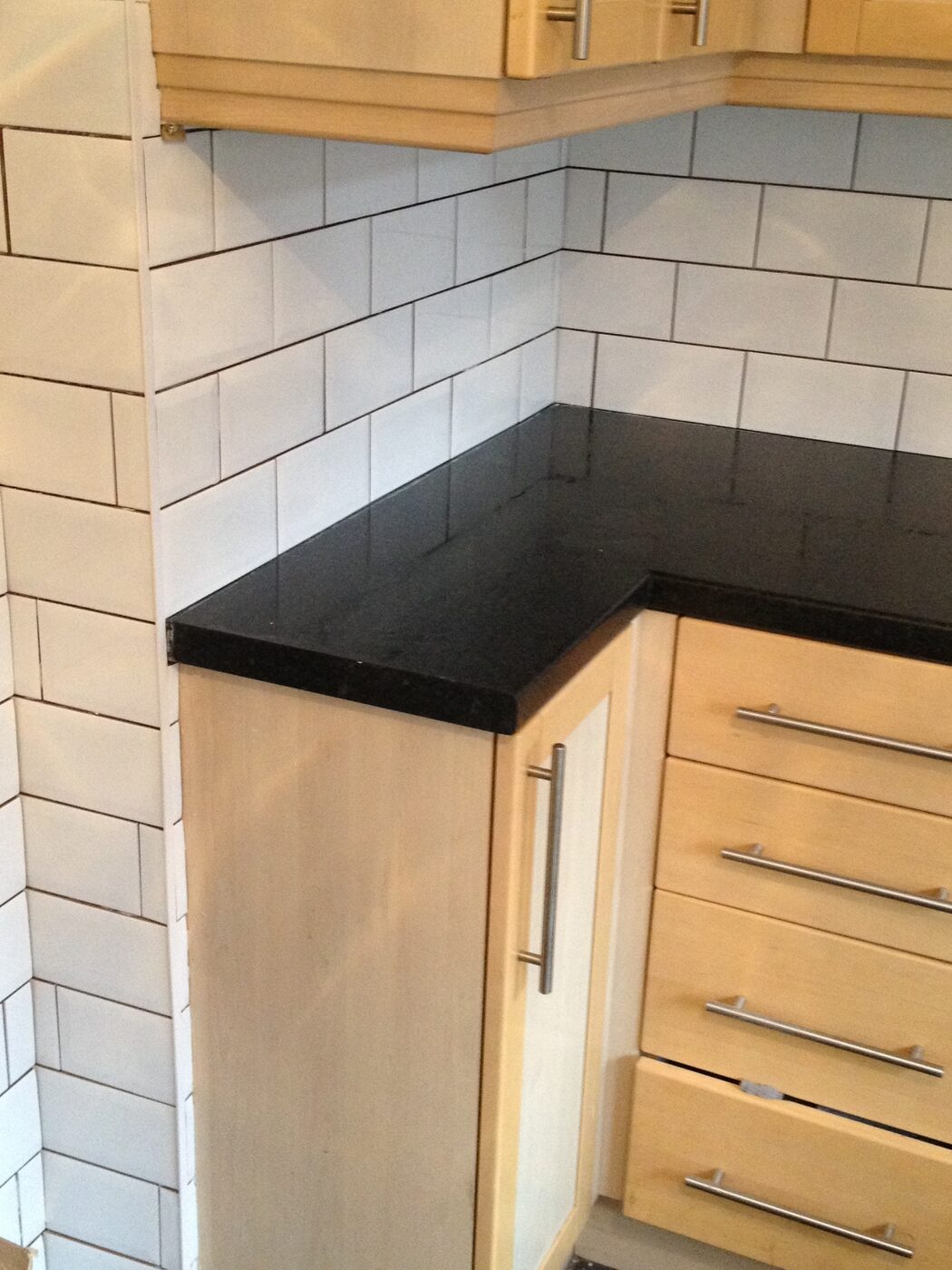 White metro tiles above a black granite worktop in a corner, with beech-fronted kitchen units below.