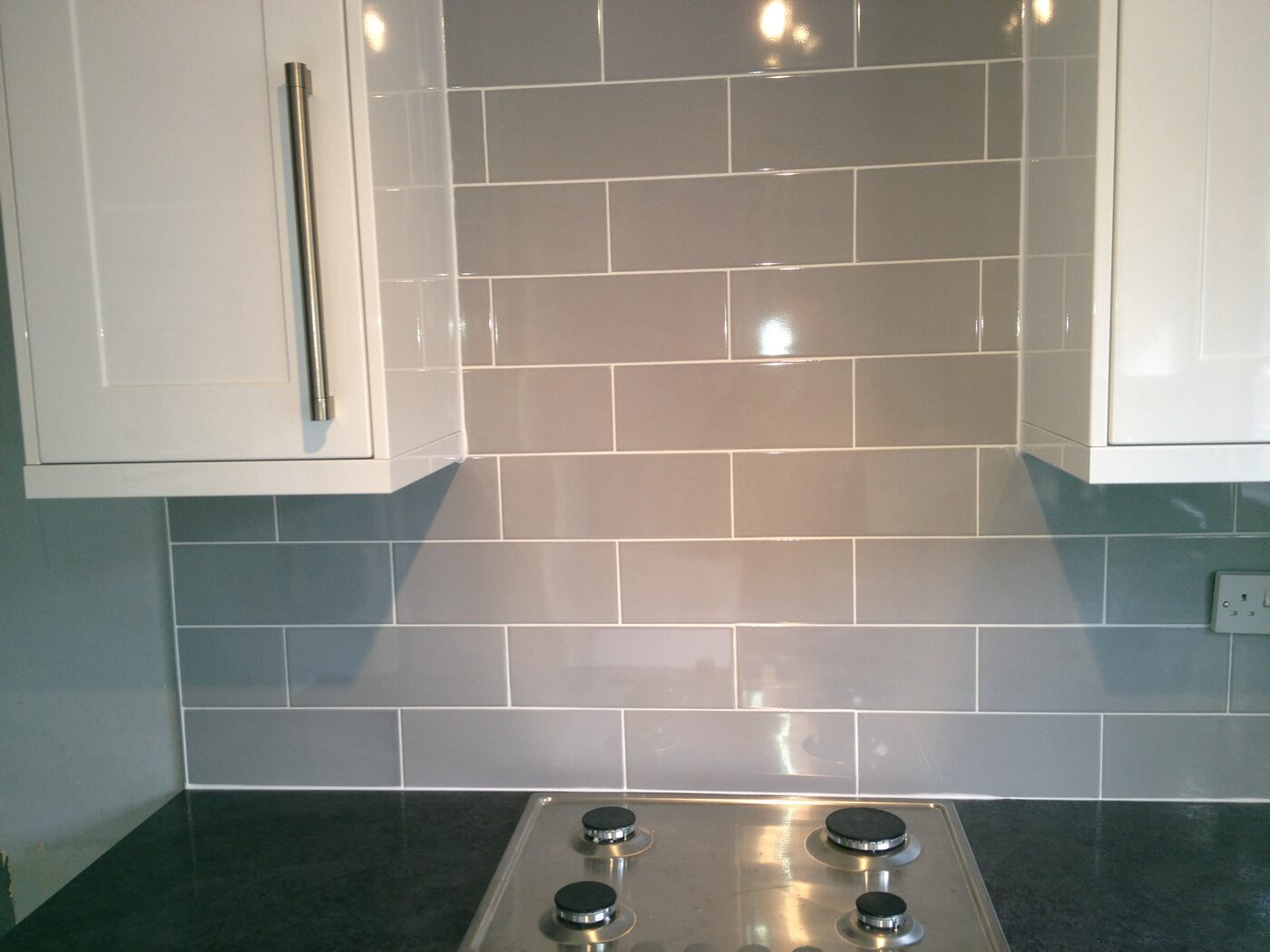 A white gloss metro tile splashback above a gas hob, running up to a wall unit.