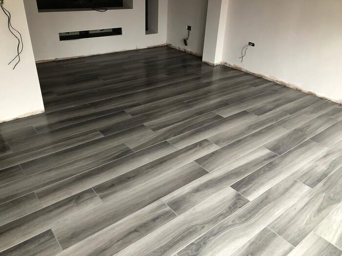 Grey wood-effect plank tiles laid across the floor of an empty room, with the walls unfinished and cables still hanging.