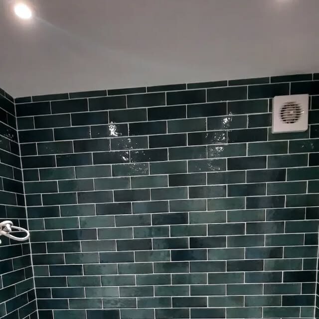 Dark green metro tiles on a shower wall, with a white extractor fan set into the tiling.