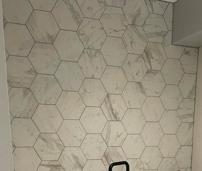 Marble-effect hexagon tiles covering a utility-room wall, cut into the corner, with the top of a black tap in front of them.